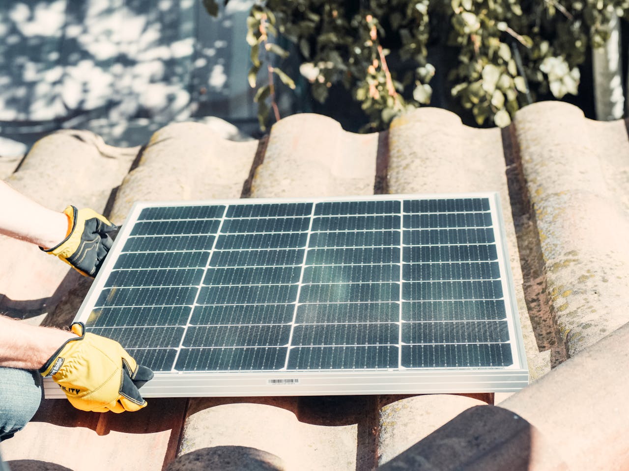 Technician fitting solar panel on rooftop in sunlight. Renewable energy installation.